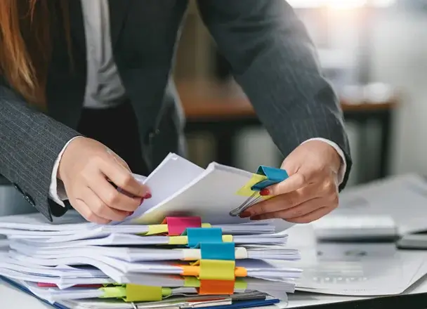 大量の紙の資料の中からひとつの資料を取り出そうとしている人の画像