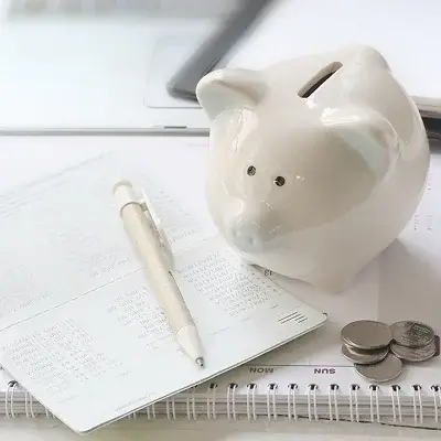 机の上に紙とペン、豚の貯金箱が置いてある写真